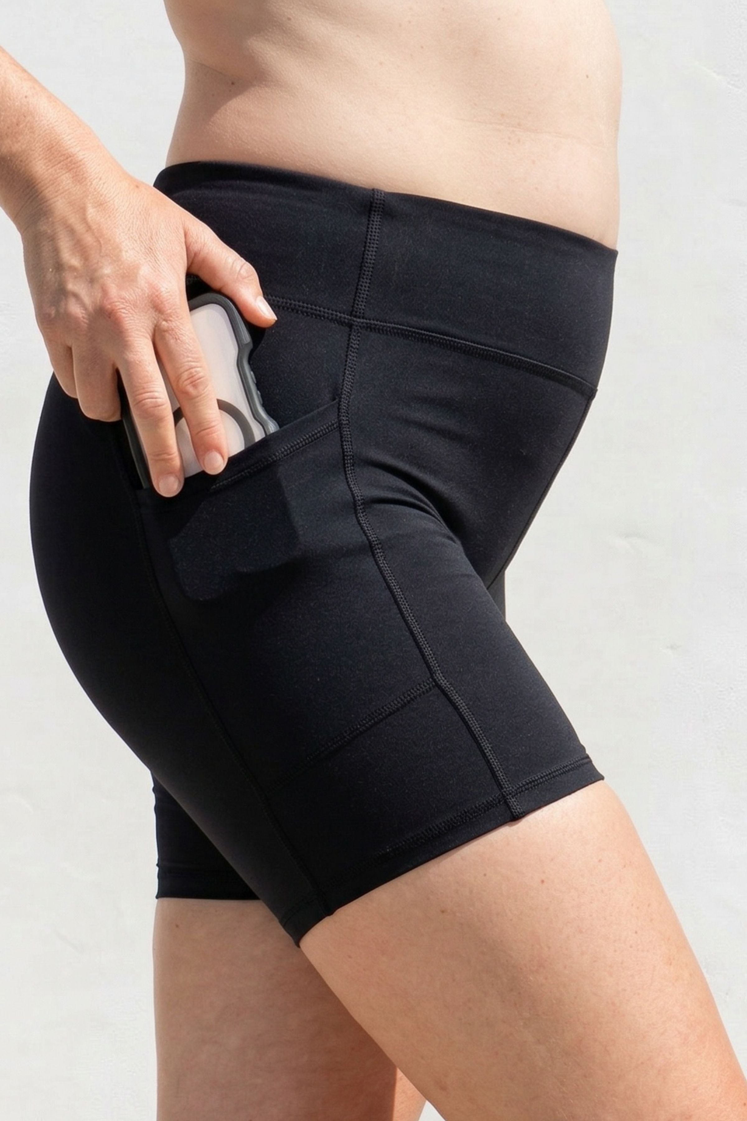 Person wearing black athletic shorts with a pocket on a light gray background