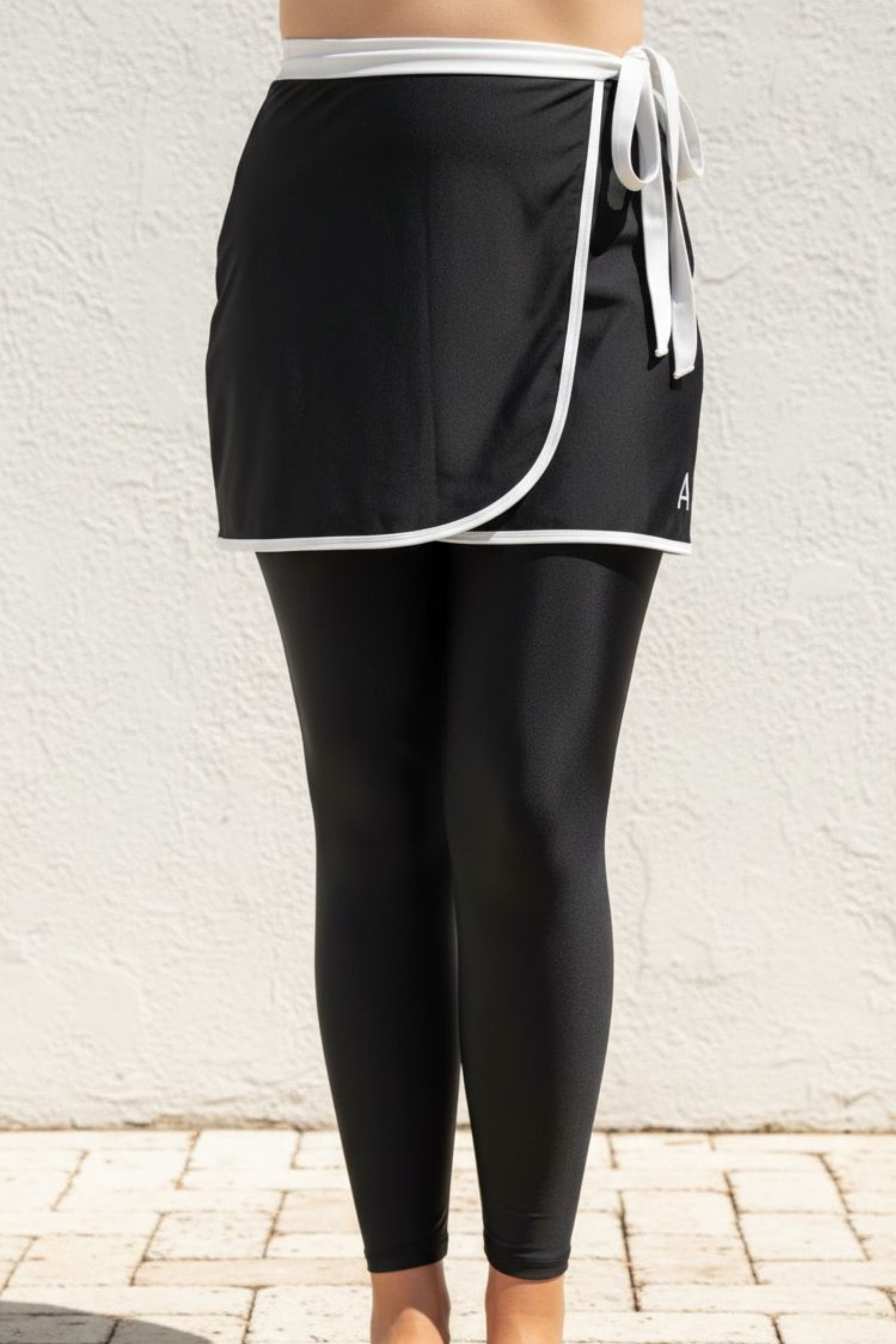 Black athletic swim skirt and swim leggings set with white trim against a light background