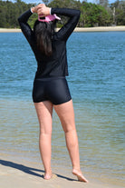 model wearing black andavi swim loose fit rash guard and matching black swim shorts with pink andavi swim logo cap