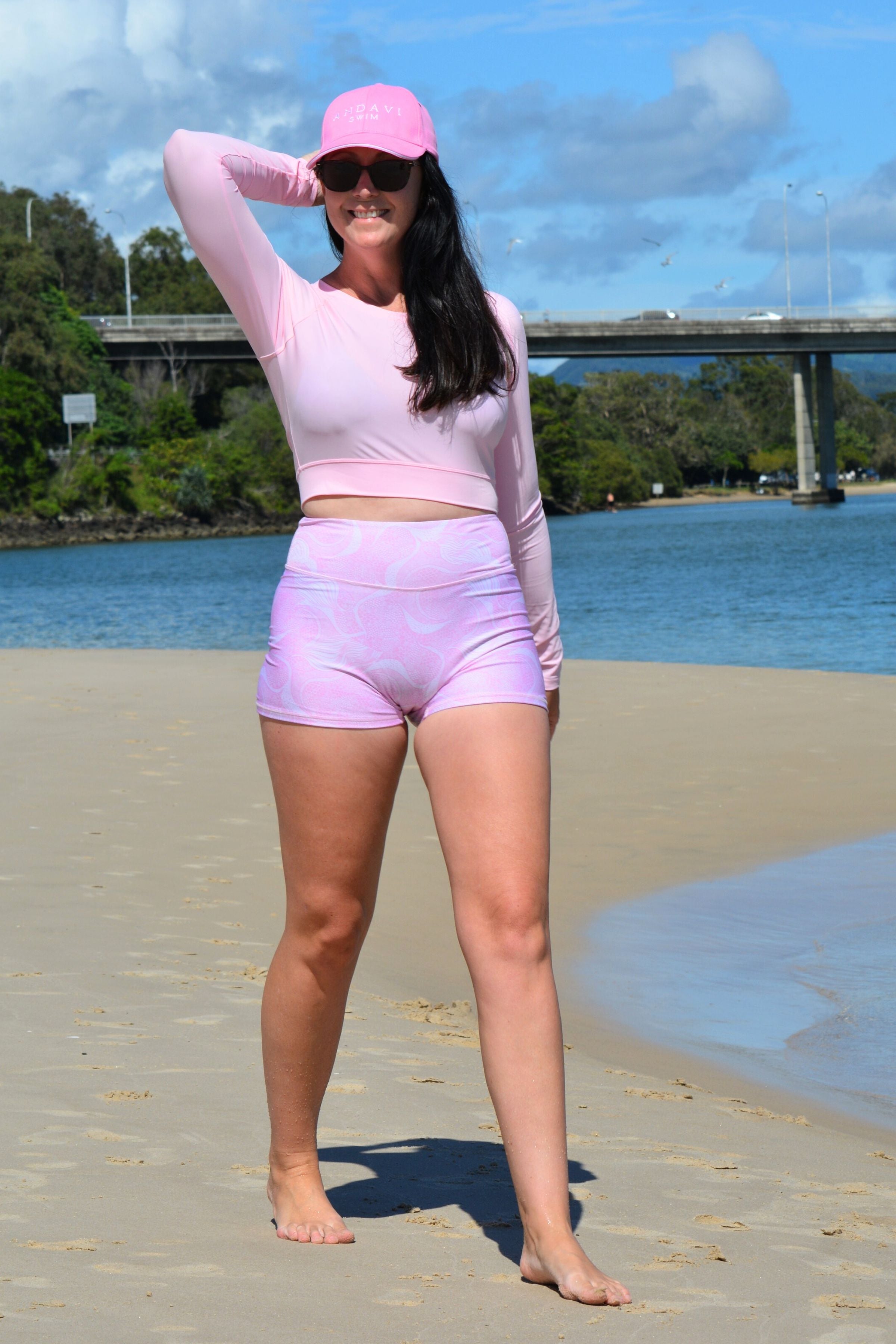 women wearing andavi swim pink crop top rash guard and pink print swim shorts and matching pink andavi swim logo cap