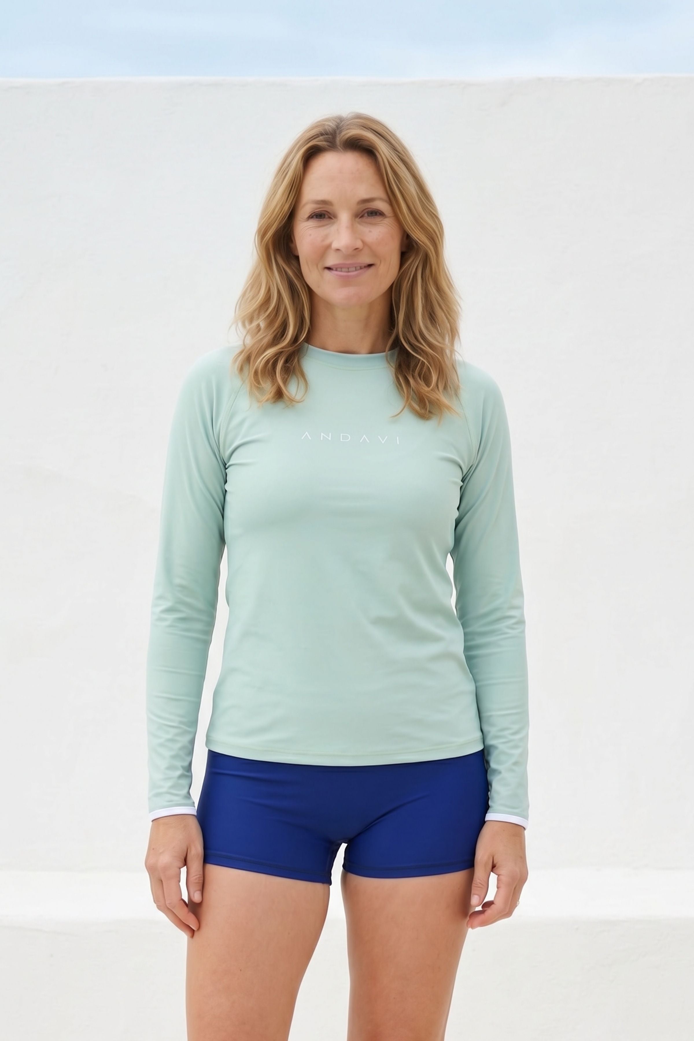 women wearing green rash guard and blue swim shorts against white wall