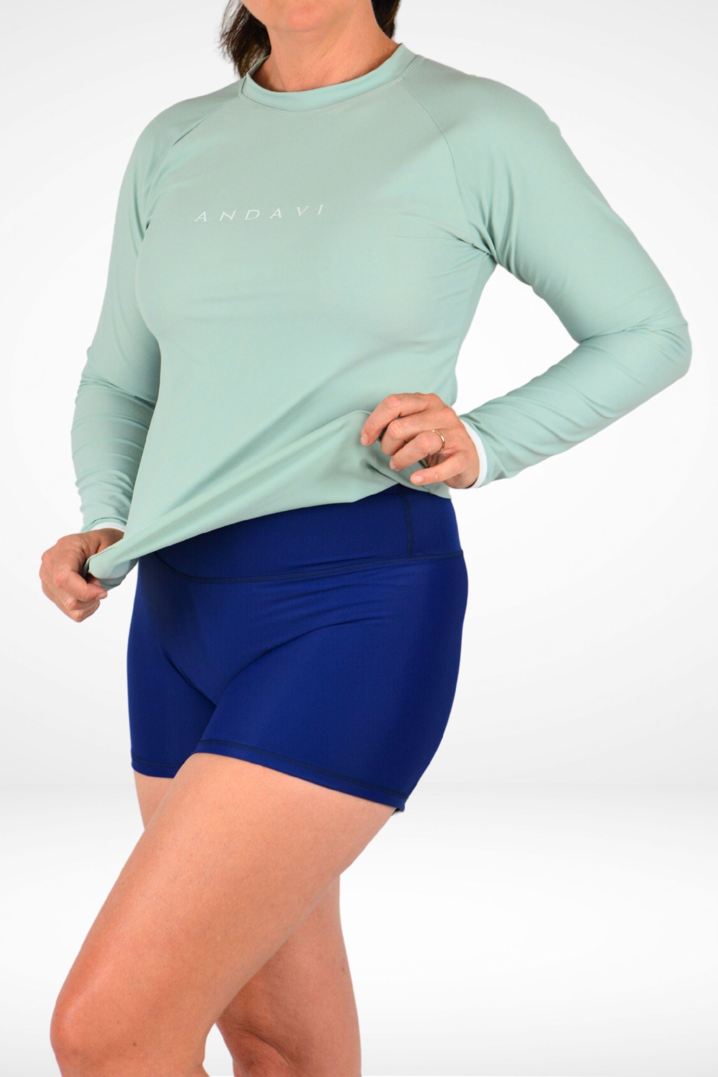 Person wearing a light green long-sleeve athletic shirt and blue shorts on a white background