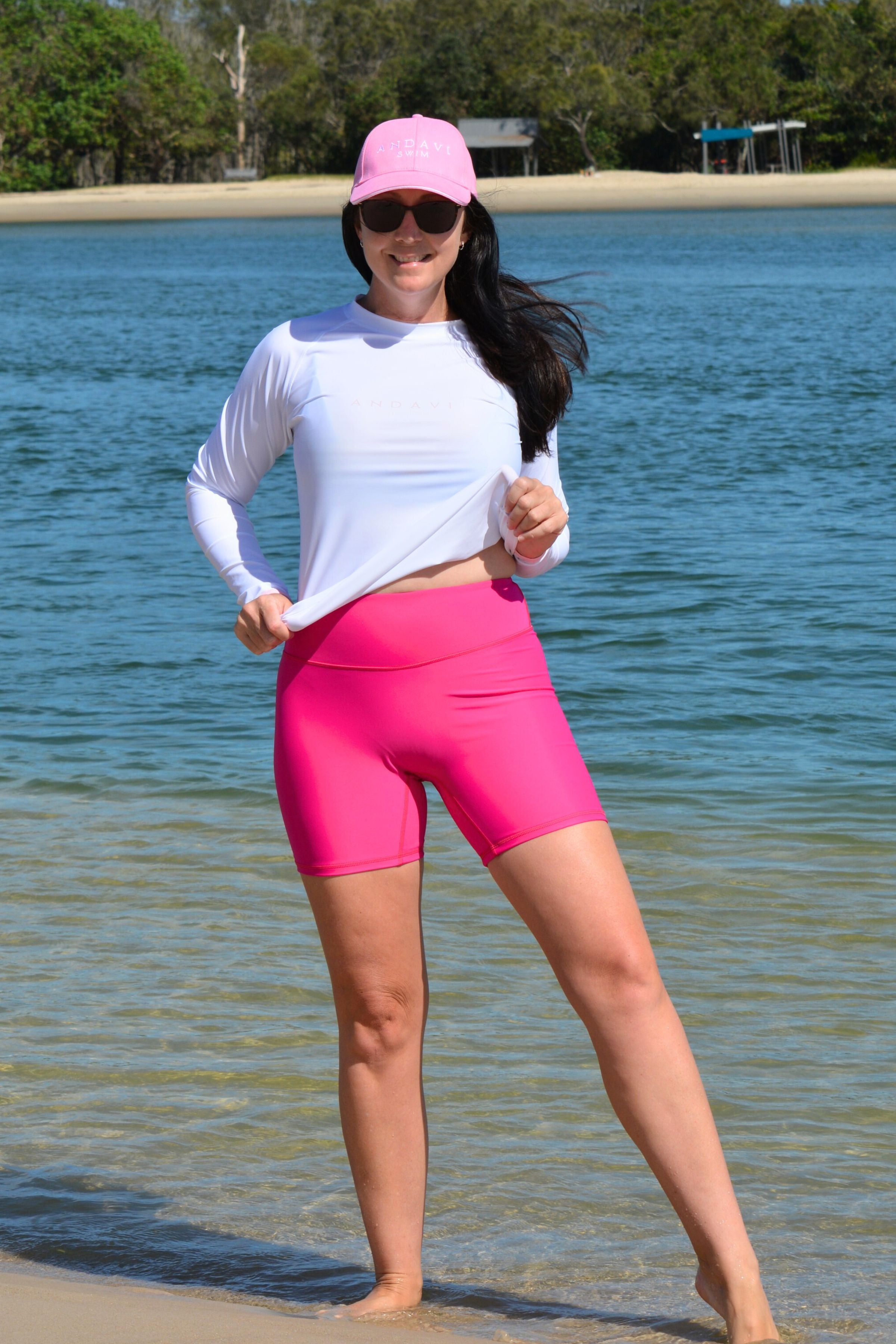 model wearing andavi swim hot pink swim shorts and white long sleeve rash guard with matching hot pink andavi swim logo cap