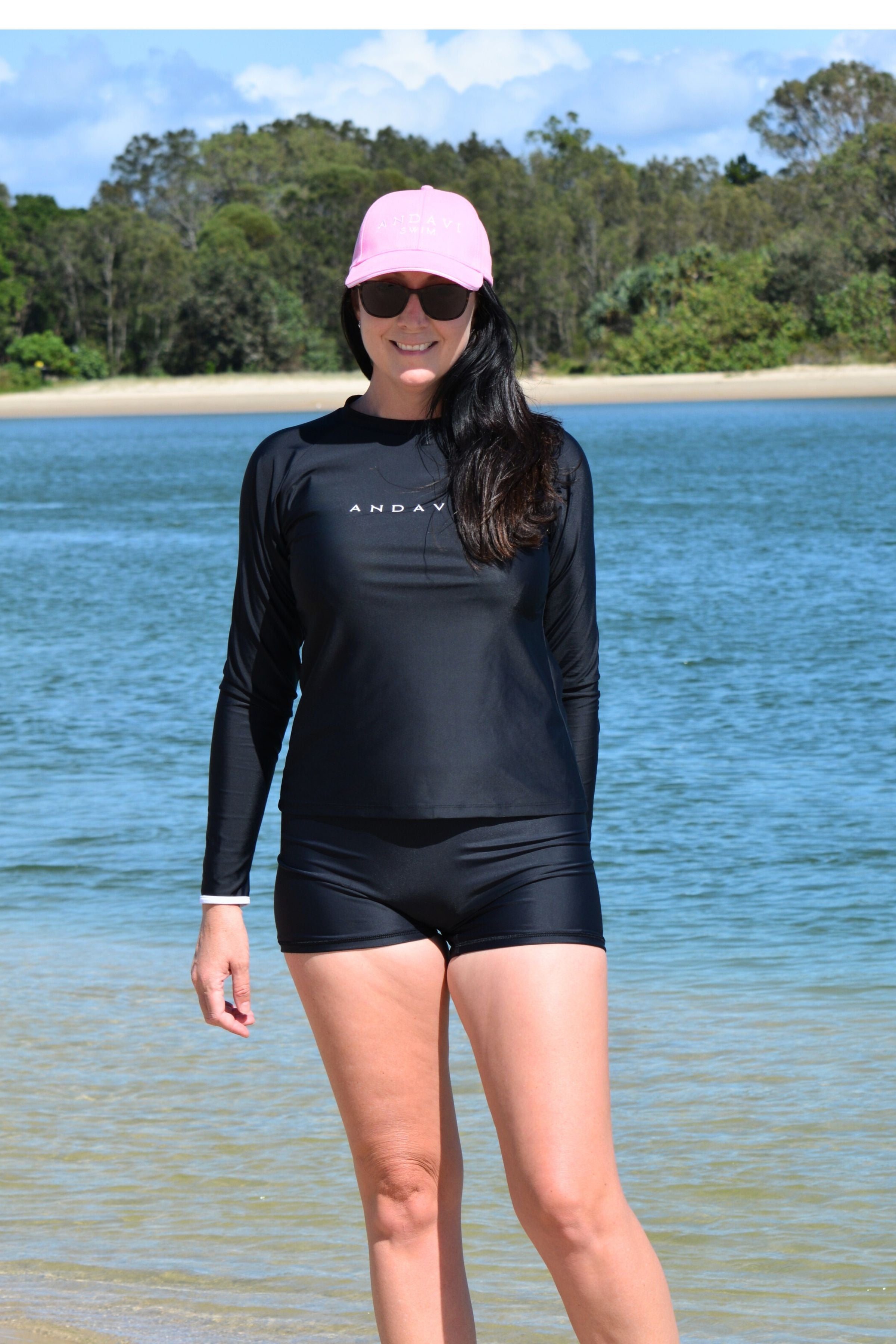 model wearing black andavi swim loose fit rash guard and matching black swim shorts with pink andavi swim logo cap