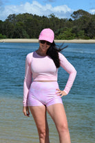 women wearing andavi swim pink crop top rash guard and pink print swim shorts and matching pink andavi swim logo cap