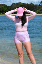 women wearing andavi swim pink crop top rash guard and pink print swim shorts and matching pink andavi swim logo cap