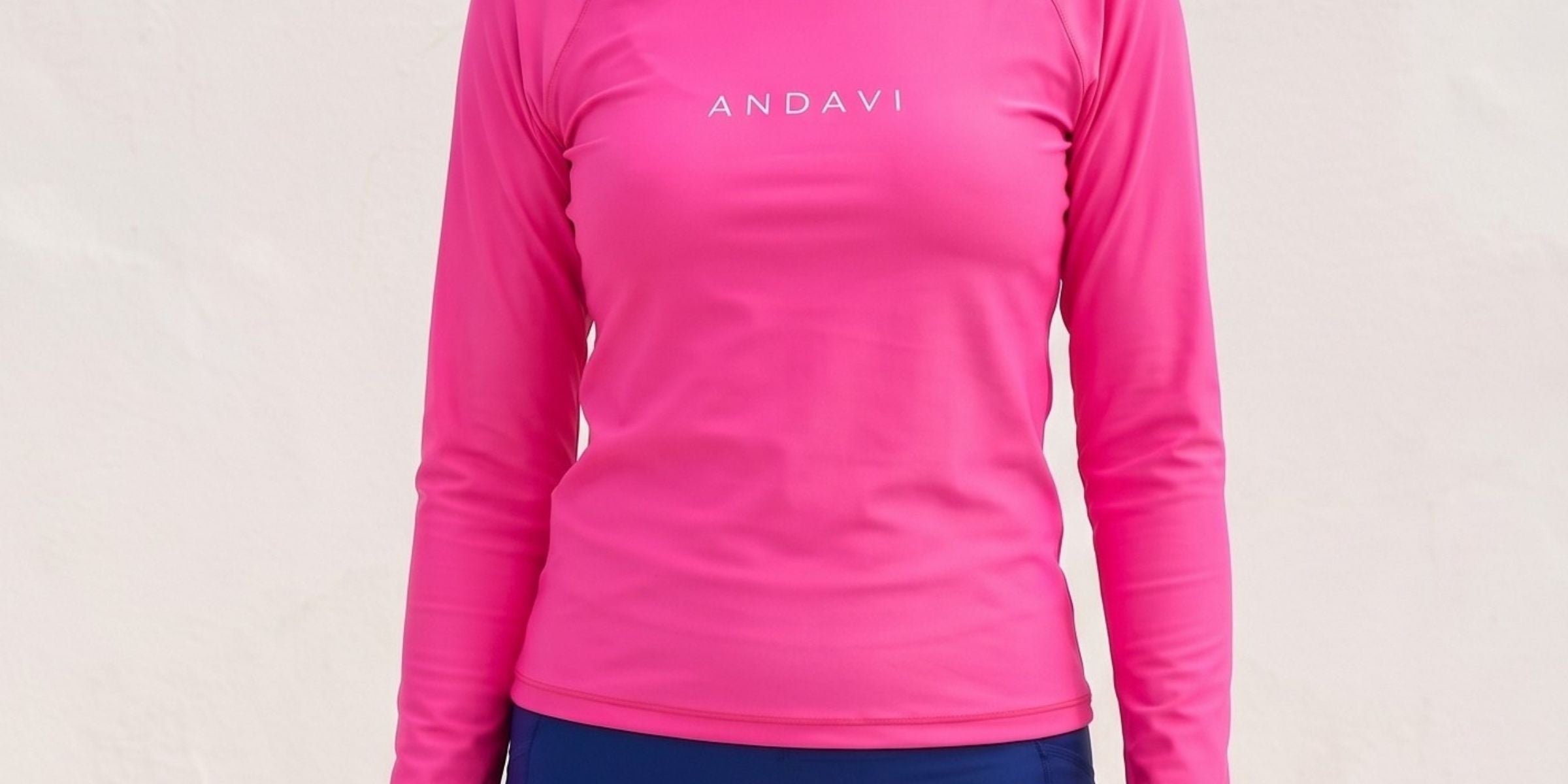 Woman wearing a pink long-sleeve shirt and blue shorts with 'ANDAVI' branding on a light background