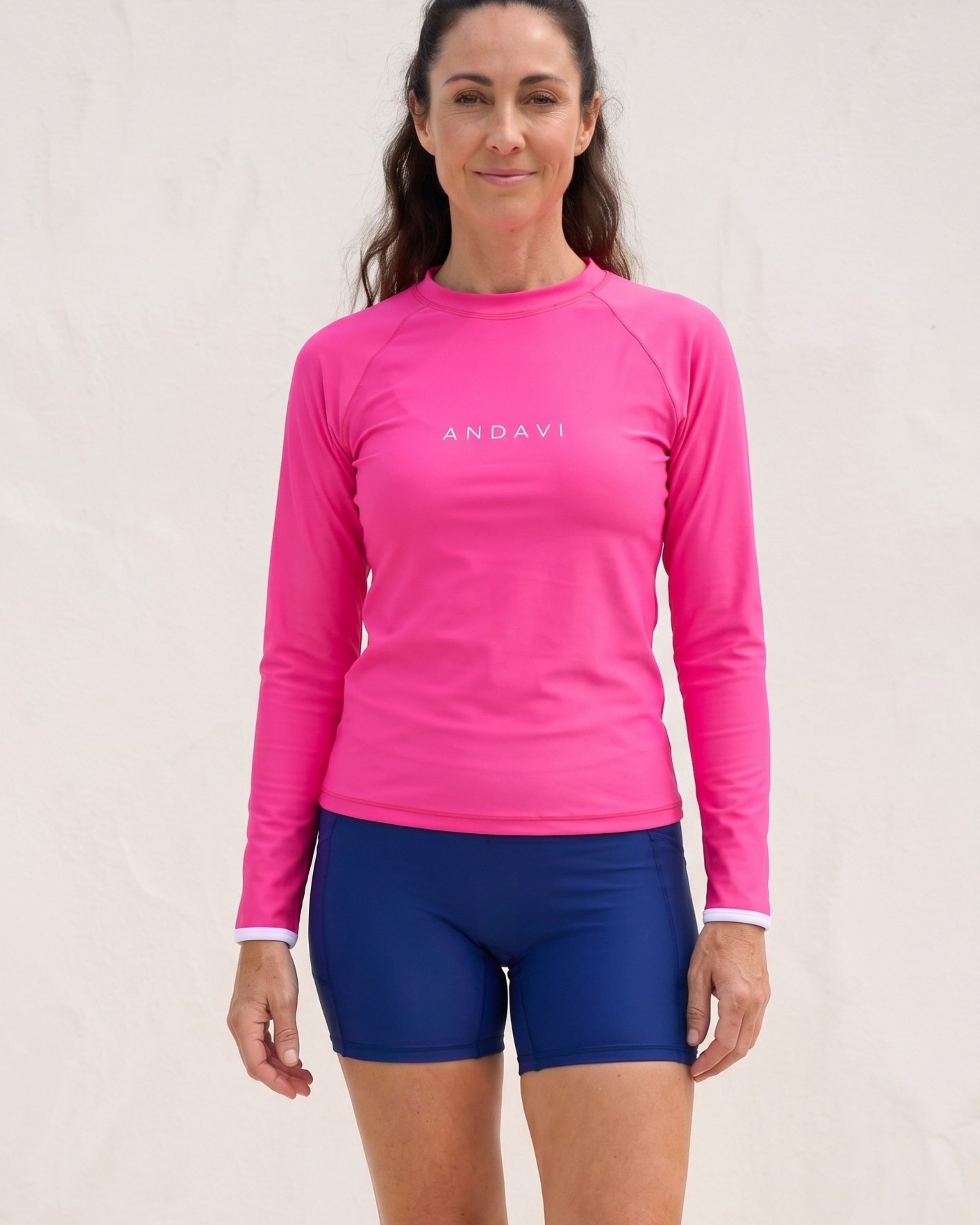 Woman wearing a pink long-sleeve shirt and blue shorts with 'ANDAVI' branding on a light background