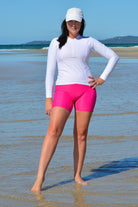 Woman in white long-sleeve top and pink shorts standing on a beach.