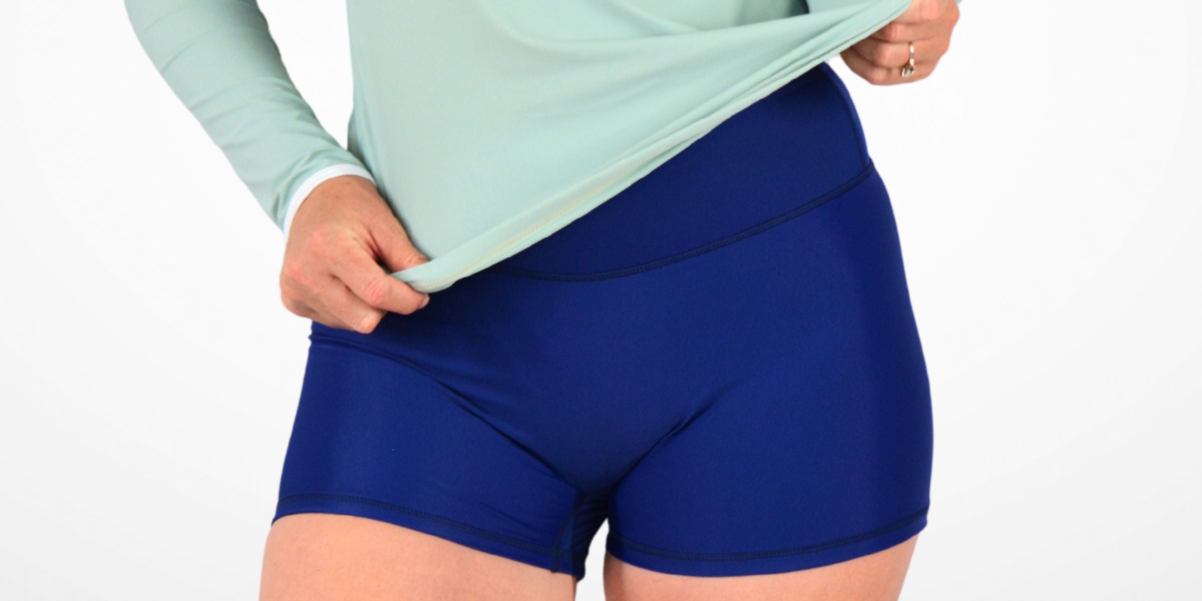 Person wearing a light green long-sleeve shirt and blue shorts on a white background