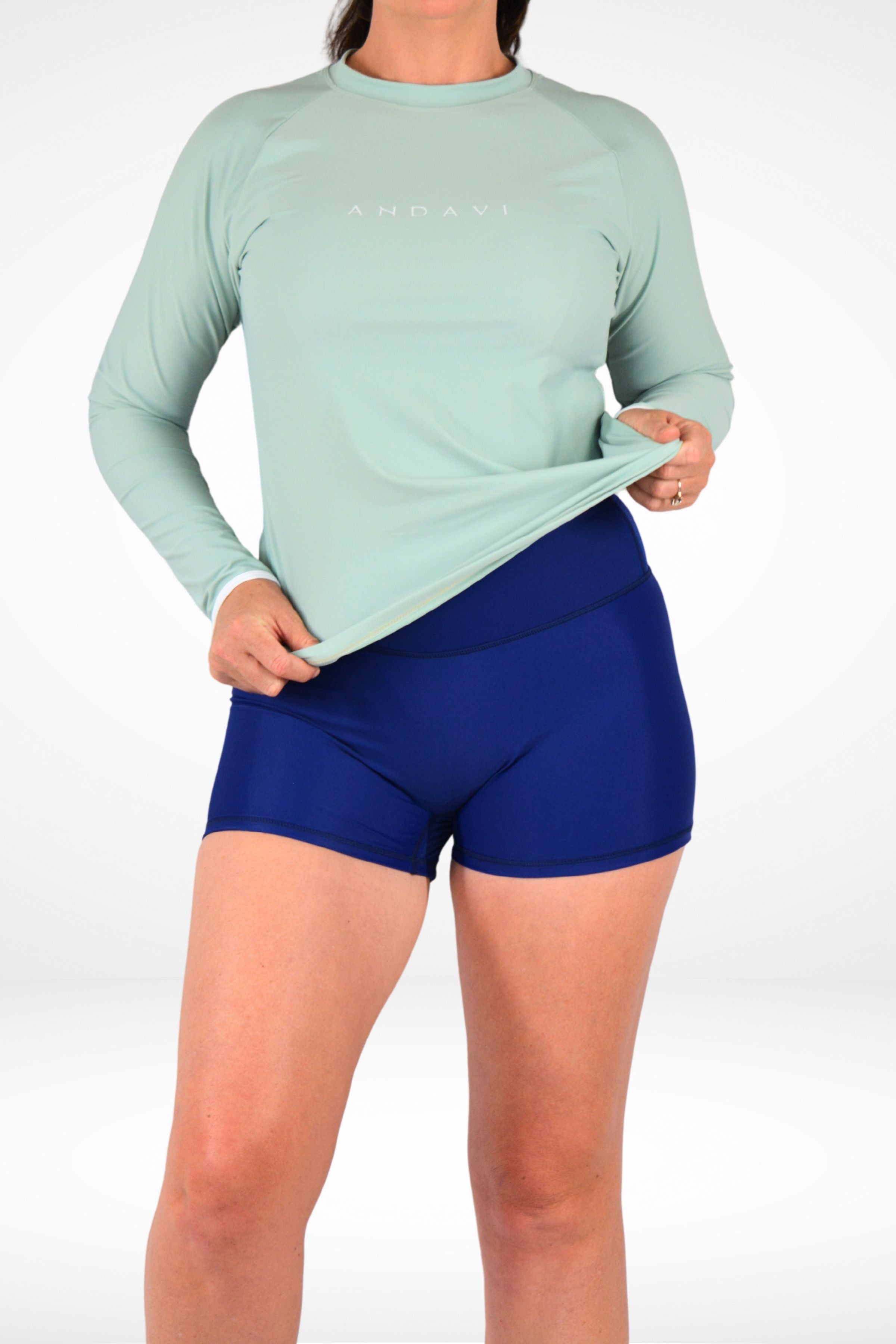 Person wearing a light green long-sleeve shirt and blue shorts on a white background