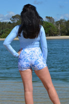model on the beach wearing andavi swim light blue long sleeve upf50+ crop top and swim active shorties in white and blue print