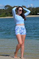 model on the beach wearing andavi swim light blue long sleeve upf50+ crop top and swim active shorties in white and blue print