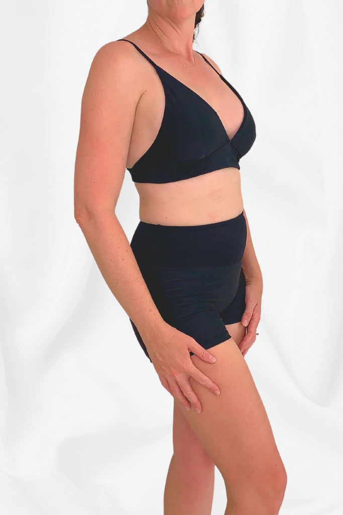 model facing side on wearing a black triangle bikini top with black swim shorts 