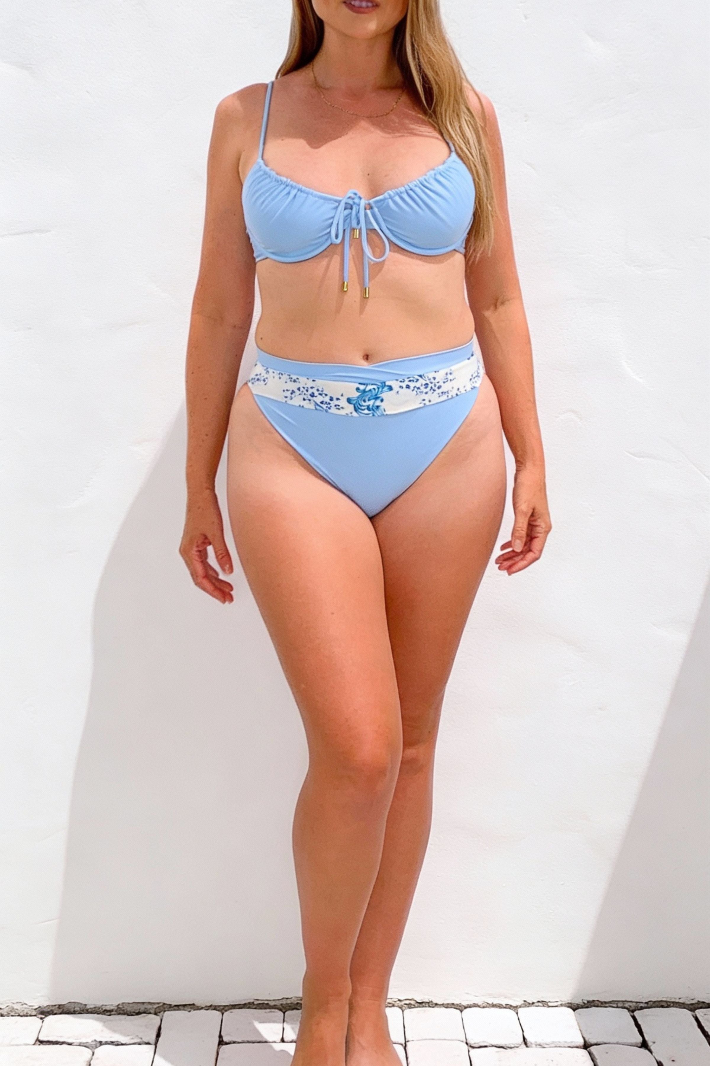 Woman wearing a light blue bikini with floral patterned bottom against a white background