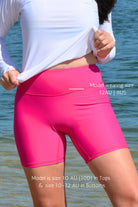 model wearing andavi swim hot pink swim shorts and white long sleeve rash guard with matching hot pink andavi swim logo cap