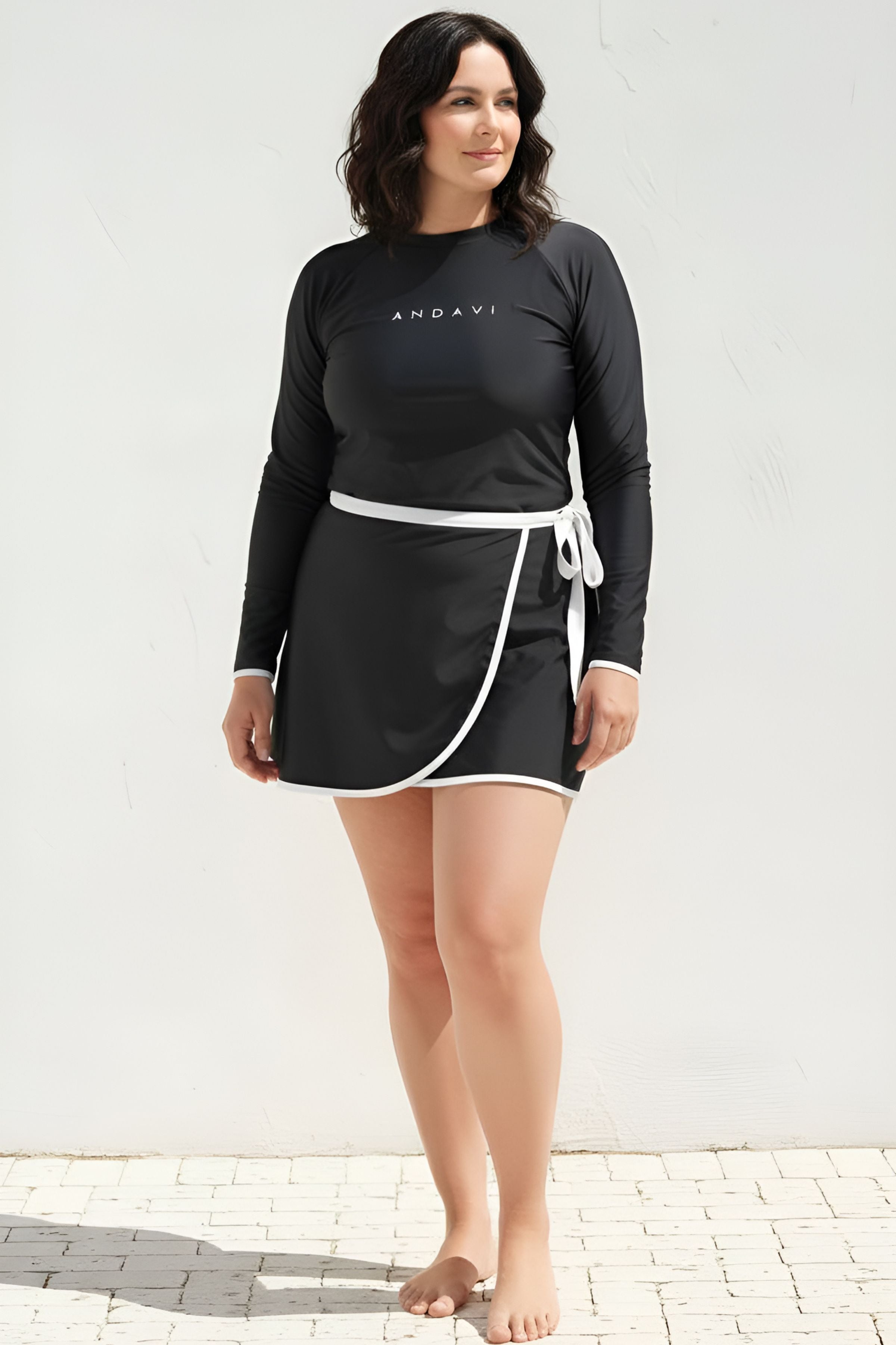Woman wearing a black long-sleeve top and skirt with a white border against a light background