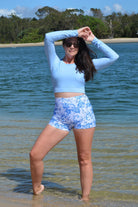 model on the beach wearing andavi swim light blue long sleeve upf50+ crop top and swim active shorties in white and blue print