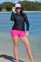 model wearing black andavi swim loose fit rash guard and matching pink swim shorts with pink andavi swim logo cap