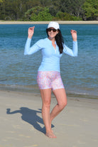 women walking on the beach wearing light blue long sleeve rash guard and floral bike shorts