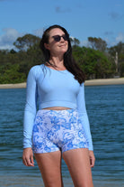 model on the beach wearing andavi swim light blue long sleeve upf50+ crop top and swim active shorties in white and blue print