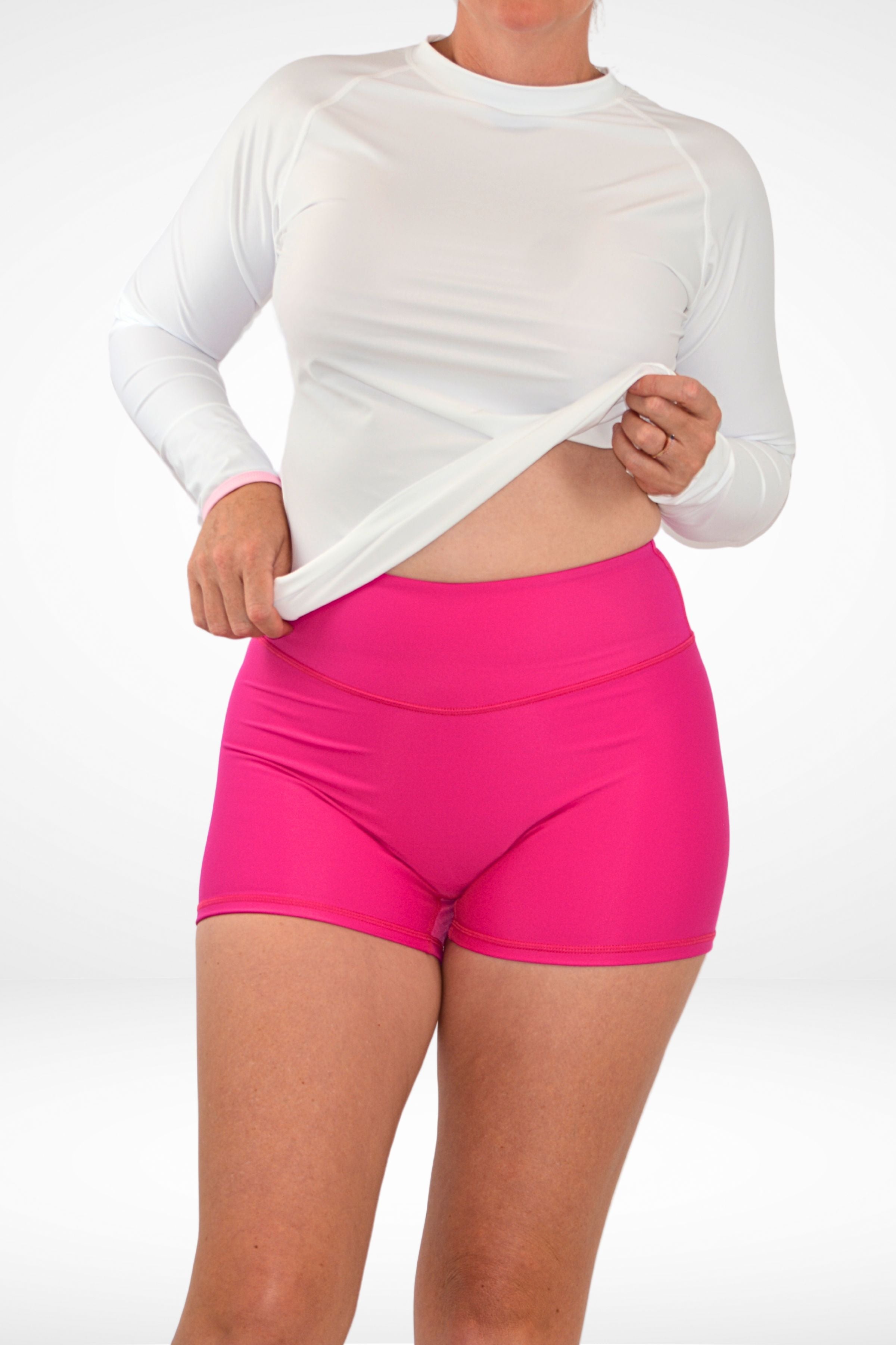 model lifting up a white rash guard and wearing high waist pink swim active shorties
