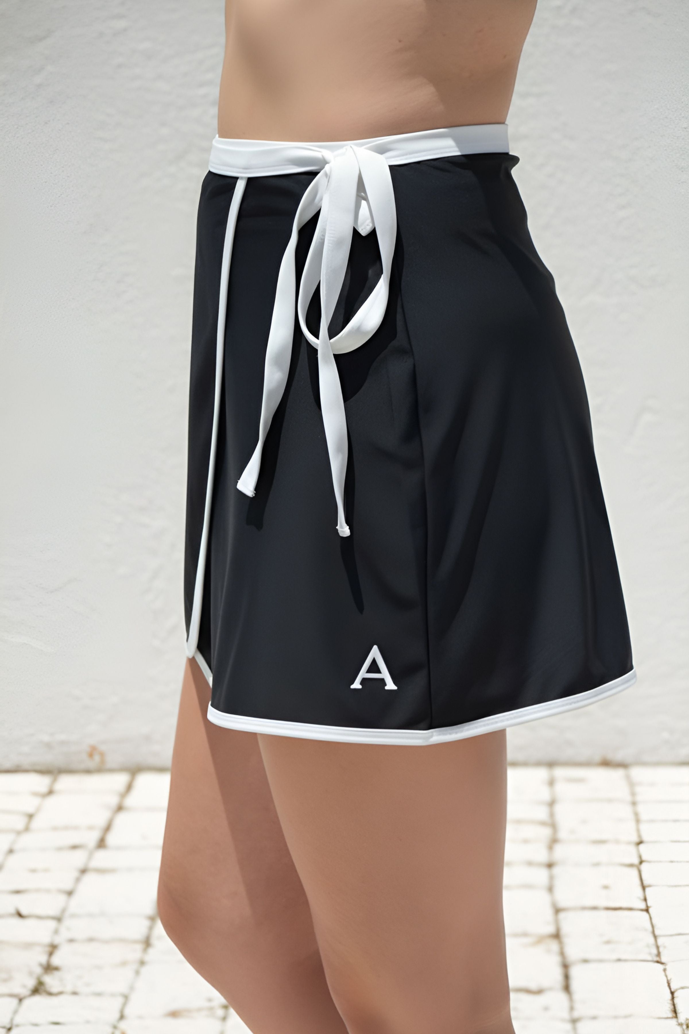 Black athletic swim skirt with white drawstring and trim on a person against a light background