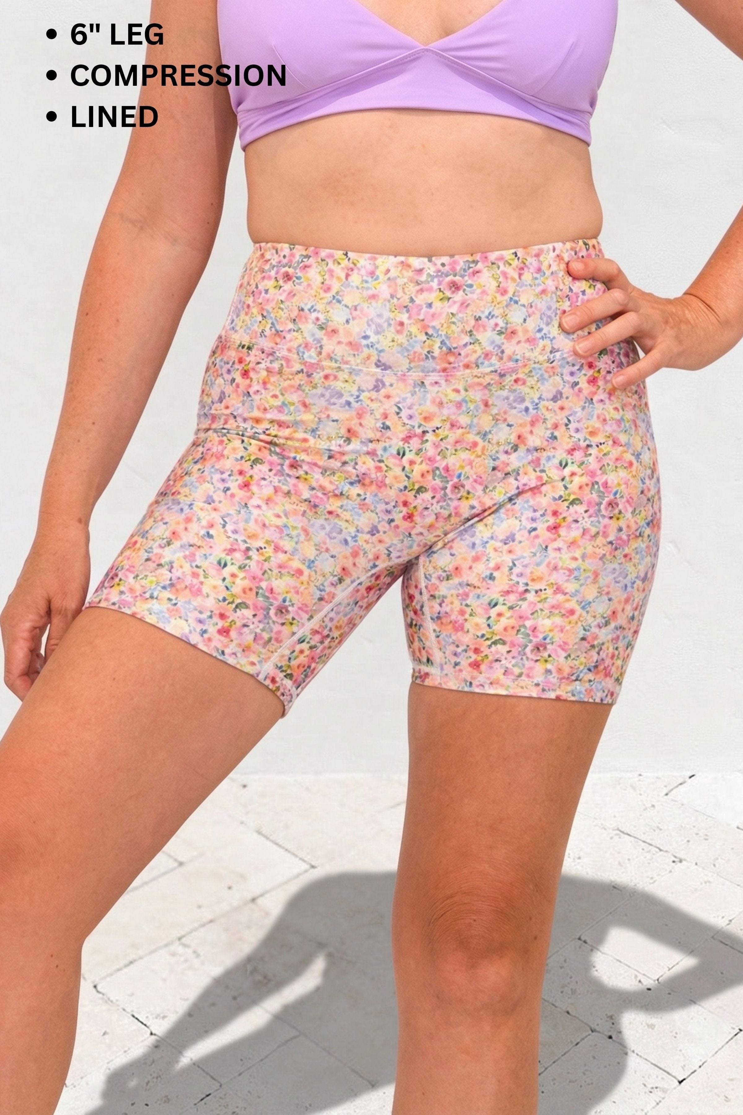 Person wearing colorful floral shorts and a purple top on a light background