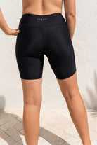 Person wearing black athletic shorts with a visible brand logo on a light background