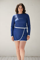 Woman wearing a blue rash guard  with long sleeves and matching blue wrap swim skirt