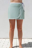 Person wearing a light green skirt with white trim against a white wall.