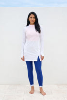 Woman wearing a white long-sleeve top and blue leggings against a light background