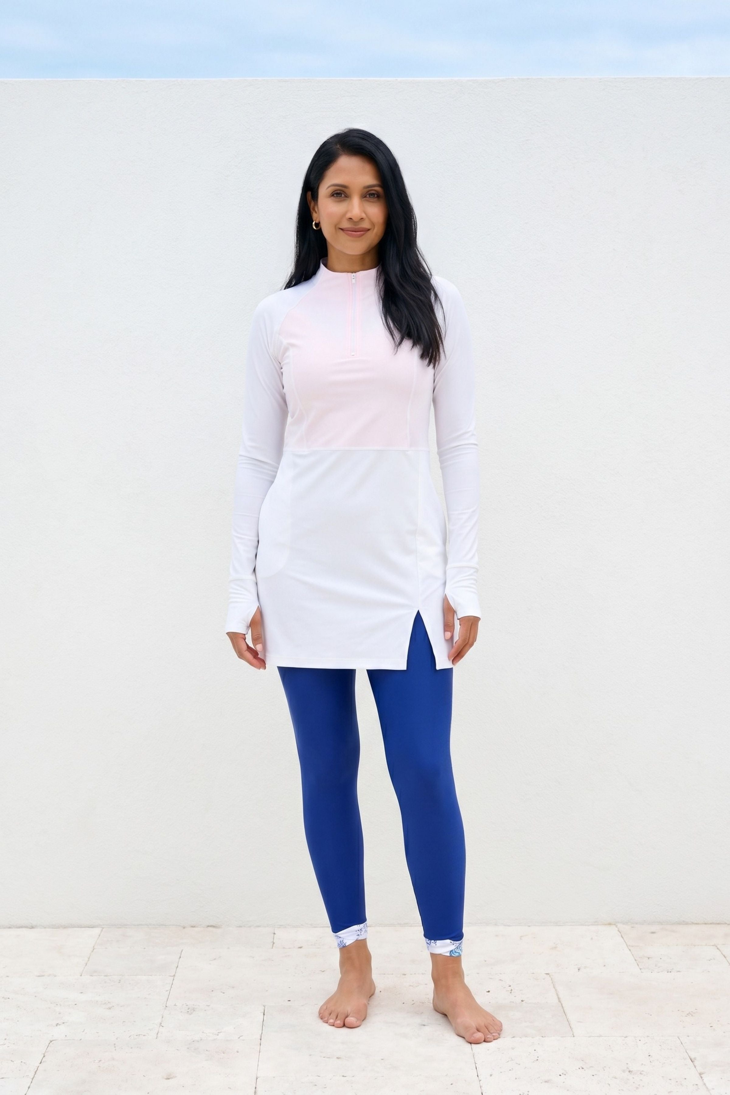 Woman wearing a white long-sleeve top and blue leggings against a light background