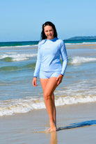 Woman in a blue swimsuit standing on a beach with ocean waves in the background