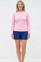 women standing in front of white textured wall wearing ligh tpink andavi rash guard and navy blue swim shorts 