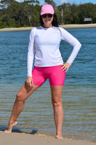 Woman in white long-sleeve top and pink shorts standing on a beach.