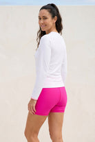 women standing in front of white wall wearing white long sleeve rash guard and pink swim shorts