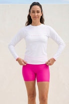 women standing in front of off white wall wearing andavi white long sleeve rash guard and pink swim shorts