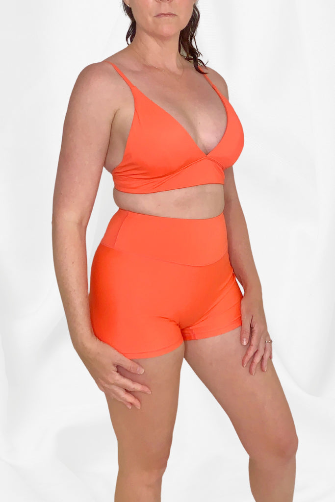 women facing side on wearing coral colour triangle bikini top and swim shorts