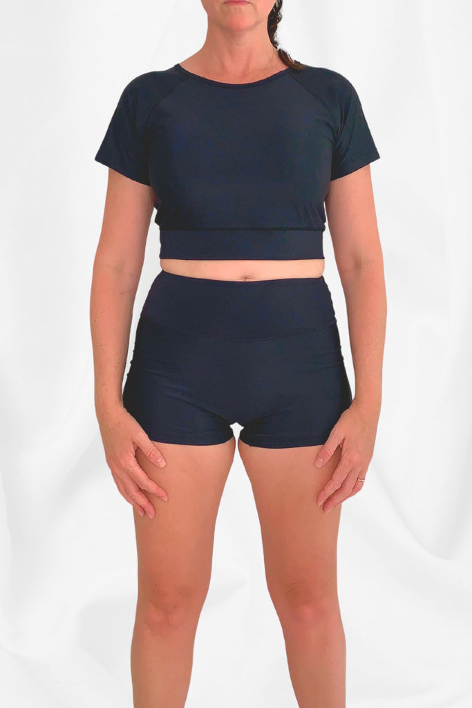 model wearing black short sleeve crop swim top and black swim shorts