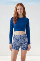 Woman wearing a blue long-sleeve top and patterned shorts on a white background