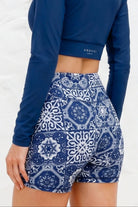 Woman wearing a blue long-sleeve top and patterned shorts against a white background