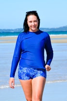 women on beach wearing dark blue long sleeve rash guard and blue and white print swim shorts