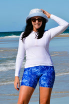 women standing ont he beach wearing bucket hat and white long sleeve rash guard with white and blue swim active bike shorts