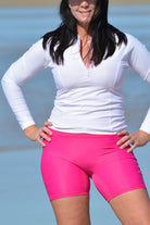 women on the beach wearing long sleeve white front zip rash guard and bright pink swim active bike shorts