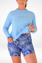 Person wearing a blue long-sleeve top and blue patterned shorts on a white background