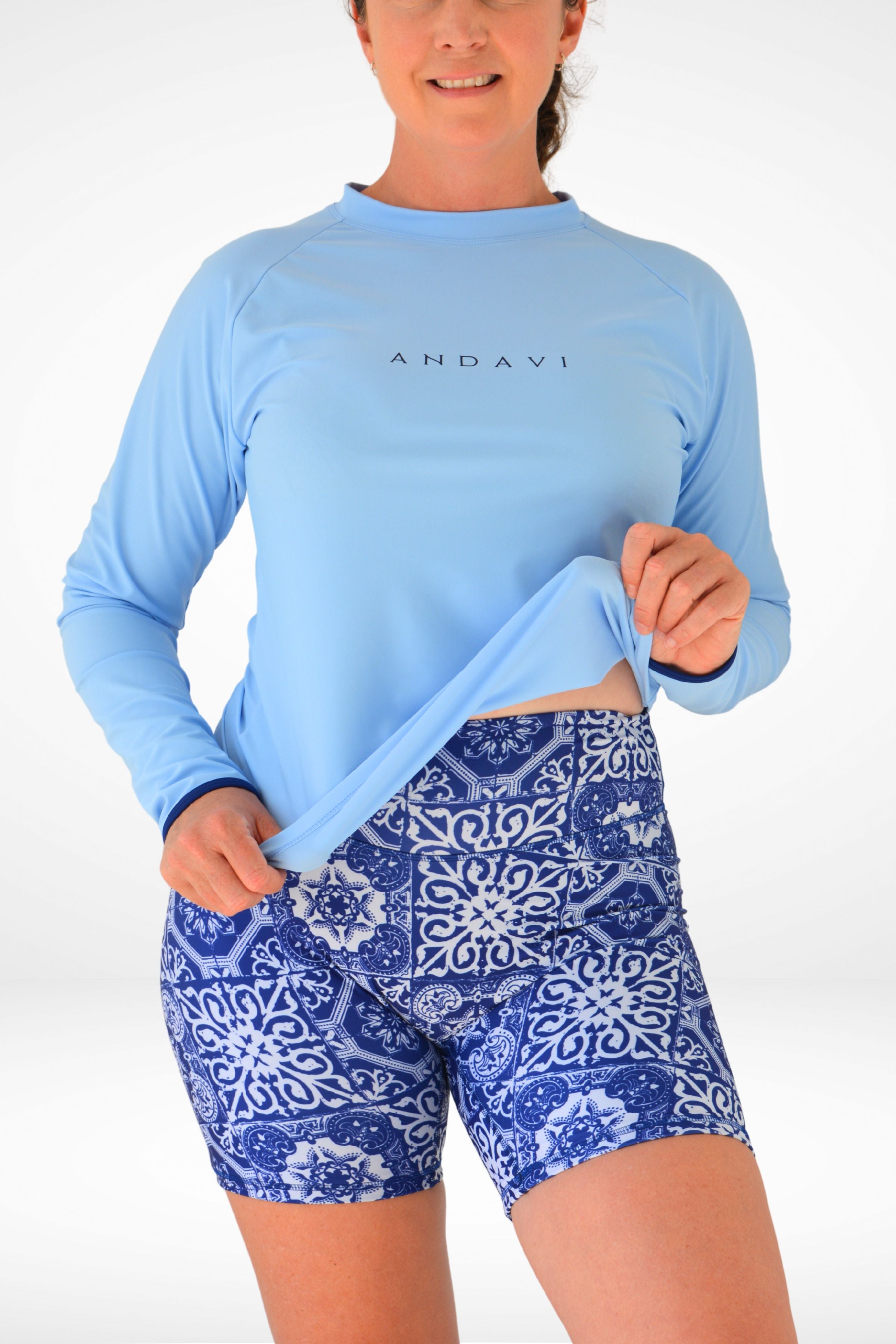 Person wearing a blue long-sleeve top and blue patterned shorts on a white background