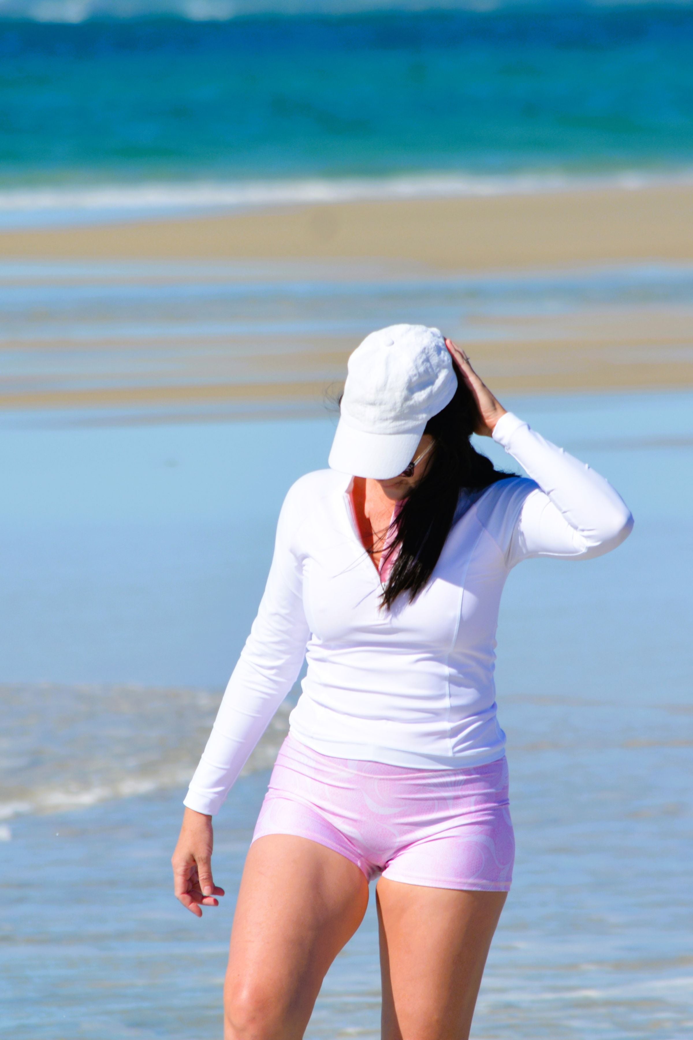 model on the beach wearing white long sleeve rash guard and white and pink print swim shorts 