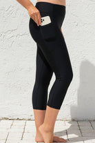 Person wearing black capri leggings with a white wall background