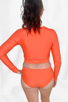 women facing away wearing andavi swim long sleeve rash guard and bikini bottom in coral colour